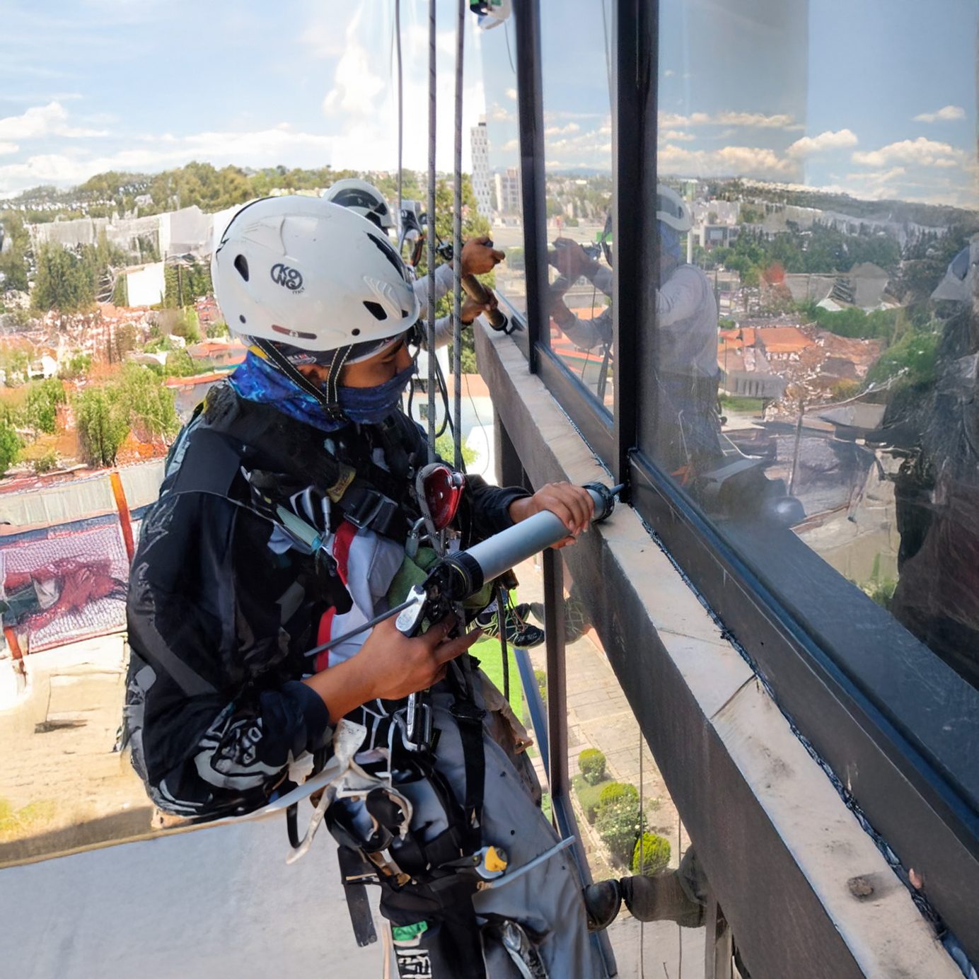 Técnico vertical sellando el marco de una ventana desde la fachada